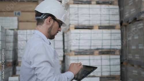 Worker male warehouse worker engineer man in a helmet working on the construction site of the warehouse, tablet computer, checking the warehouse, inspection of goods