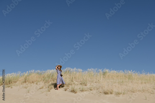 Back view of adult woman in straw hat and dress with camera standing in hill