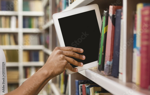 Afro student placing digital tablet on bookshelf