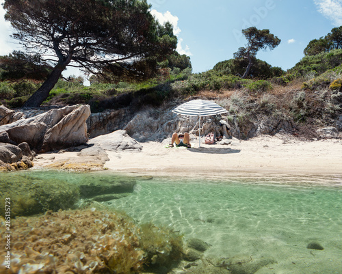 Tanned man enjoying rest under parasol in splendid place with crystal water and sandy beach in summer day, Halkidiki, Greece
