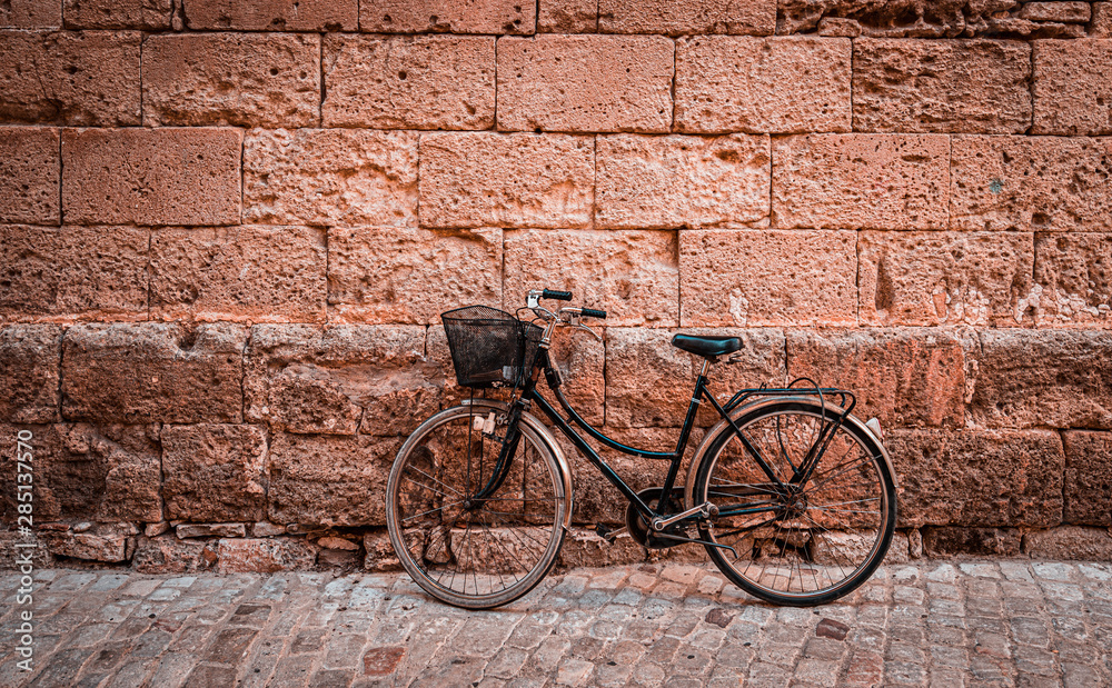 Black vintage bicycle parked against an old stone wall in Ciutadella, Minorca island in Spain.