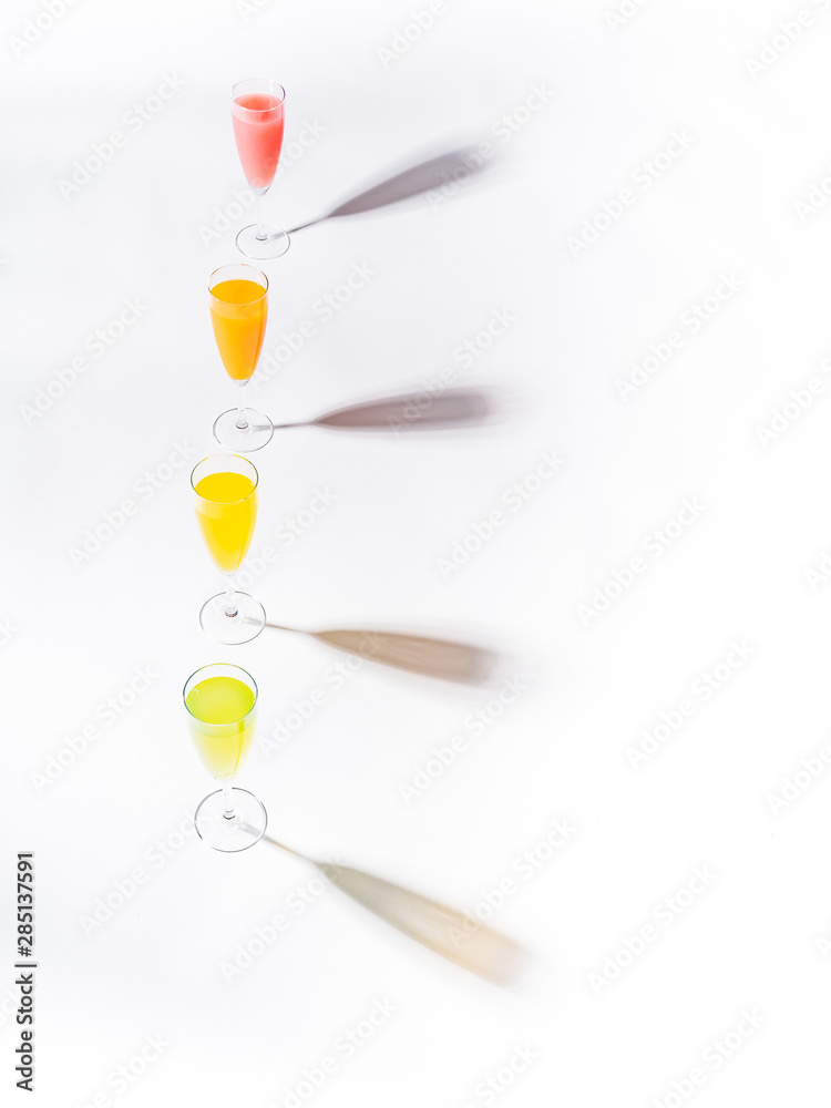 Contrasting shadows from glasses of juicy appetizing orange red yellow green drinks on white background Contrasting shadows from glasses of juicy appetizing orange red yellow green drinks on white background