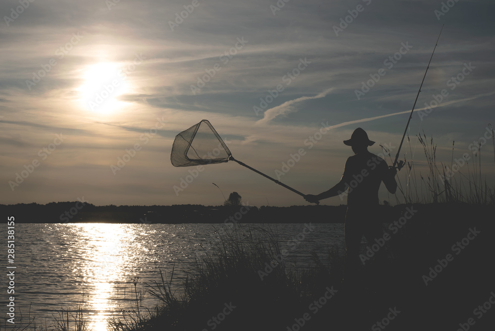 Fisherman silhouette with a rod on the pond.