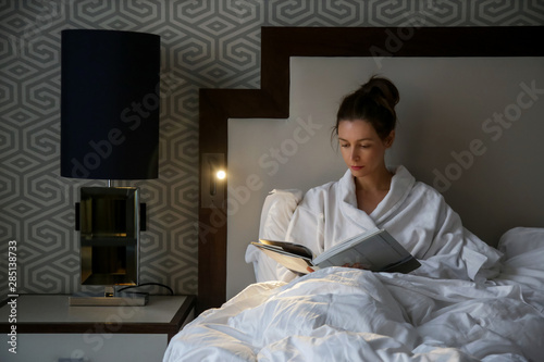 Beautiful young woman reading a book in bed 