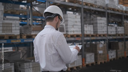 Employee male warehouse worker engineer man in hard hat working at construction site warehouse, walking in logistics center factory, engineer using tablet computer, architect businessman man indoors