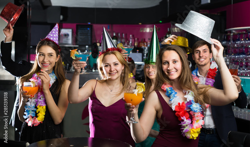 Portrait of young positive women and men in caps with cocktails