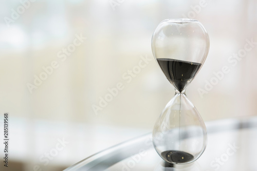 black sand hourglass with blurry background close-up on the table