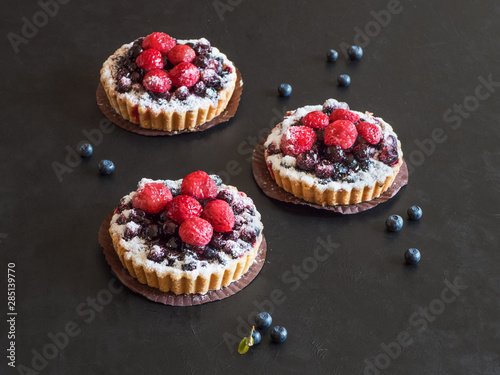 Beautiful delicious tarts, colorful pastry cakes sweets with fresh raspberries and blueberry on black background
