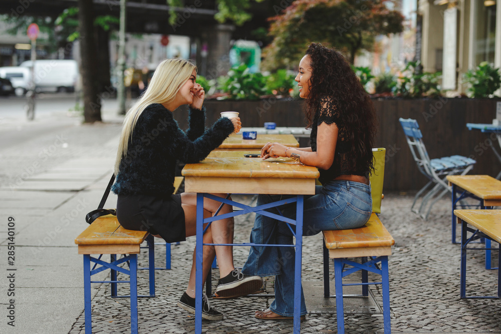 Side view of beautiful young women sitting in Berlin street cafe talking and laughing Side view of beautiful young women sitting in Berlin street cafe talking and laughing