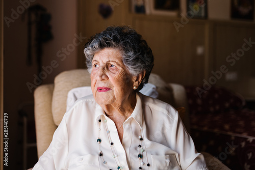 Portrait of happy senior curly gray haired woman in white shirt and with beads on neck looking away at home photo