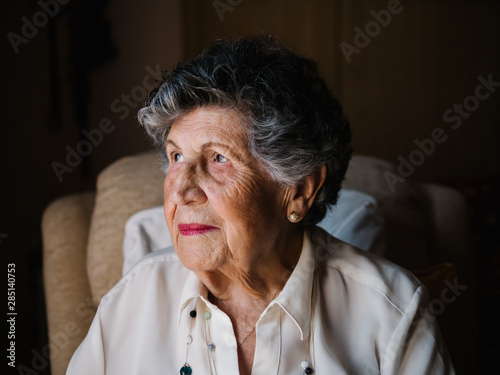Portrait of happy senior curly gray haired woman in white shirt and with beads on neck looking at camera at home photo