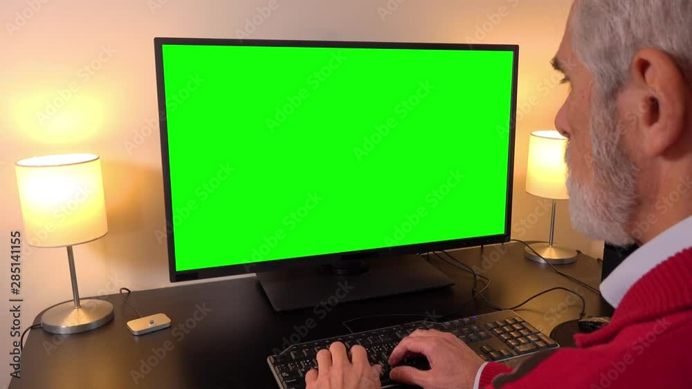 An elderly man works on a computer with a green screen in an apartment - closeup - types on keyboard An elderly man works on a computer with a green screen in an apartment - closeup - types on keyboard