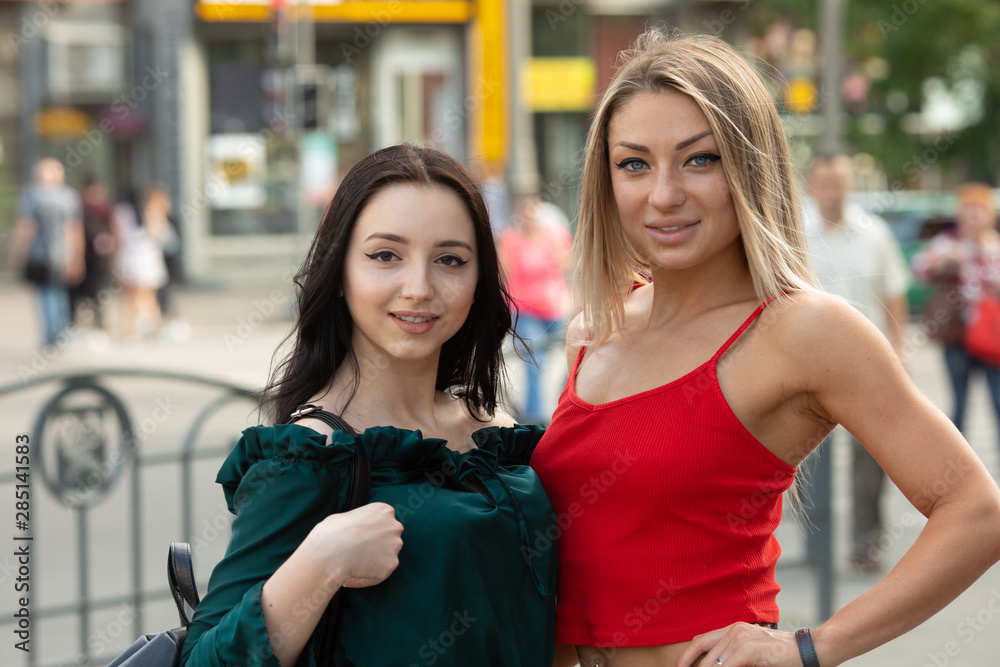 Portrait of two young beautiful blond and brunette smiling hipster girls in trendy summer clothes. Sexy carefree women posing on street background. Positive models having fun. Hugging.