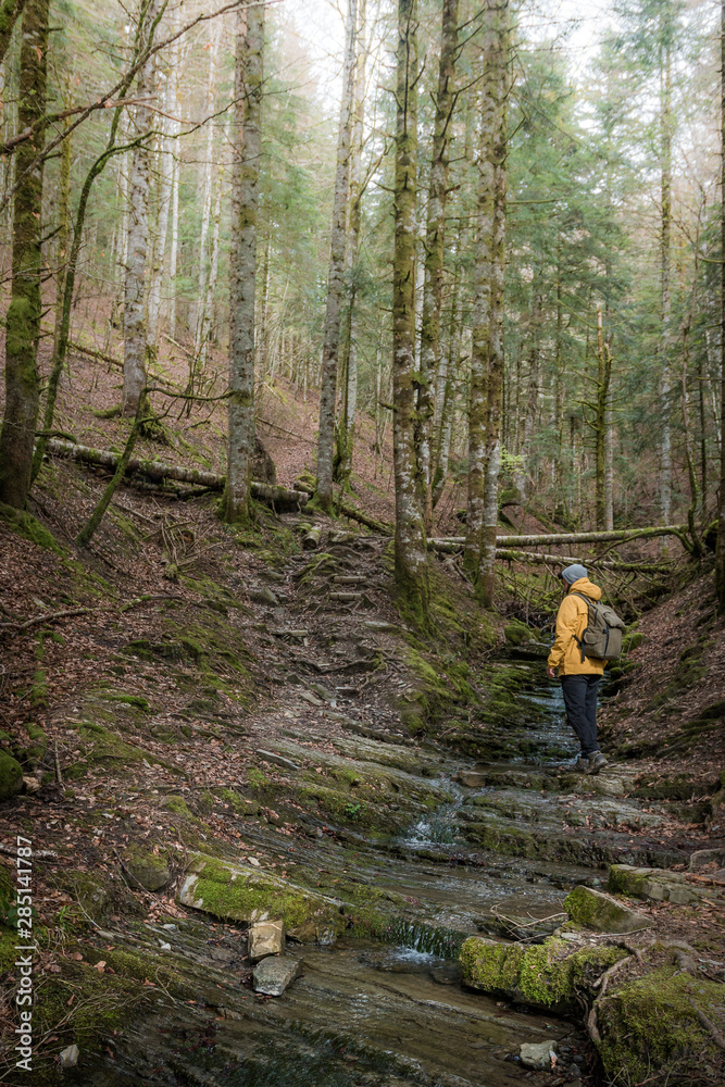 Side view of anonymous man with backpack standing on natural steps with flowing water and in mountainous terrain Side view of anonymous man with backpack standing on natural steps with flowing water and in mountainous terrain