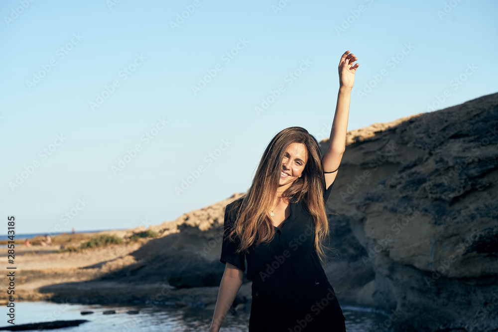 Young long haired stylish pensive female model looking at camera standing in sunlight with hills on background Young long haired stylish pensive female model looking at camera standing in sunlight with hills on background