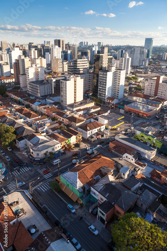 Aerial view of streets and avenues in Pinheiros neighborhood with commercial buildings and small houses at dusk on sunny summer day. The neighborhood has old houses and modern office buildings.