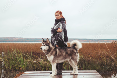 redhaired caucasian woman owner with her malamute grey big dog near the lake