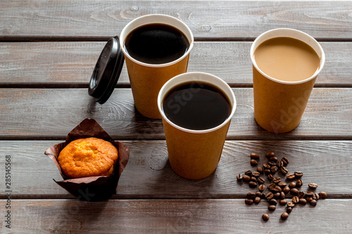 paper cups with black coffee and cappuccino to take away, beans, muffin on wooden background