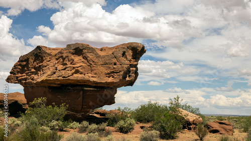 Great formation of clay and compacted sand, generated by the erosion of water and wind. Arid landscape with several bushes and large white clouds in the background.