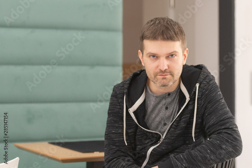 Photo shoot in cafe. Determined man. Man sitting, looking at the camera, right. On a chair, half turned.
