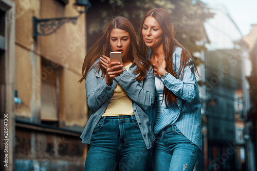 Two young women using smartphone in the street and look very surprised of what they see © mrbigphoto