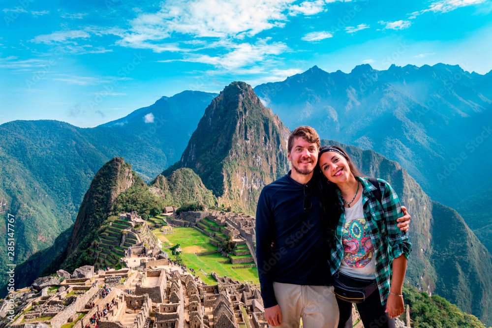 Naklejka premium Young couple of tourist in Machu Picchu. They are together, happy and relaxed. Behind, The City of Machu Picchu and the Huayna Picchu Mountain. Archaeological site, UNESCO World Heritage