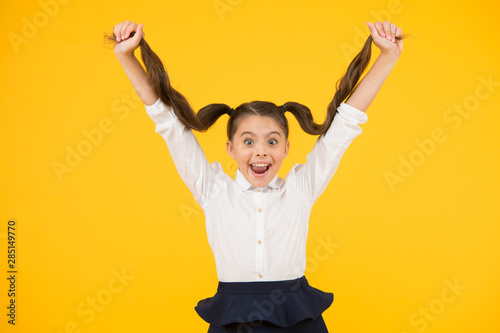 Easy hair for school. Happy small girl holding long brunette hair on yellow background. Styling hair for school in beauty salon. Her hair is her inspiration