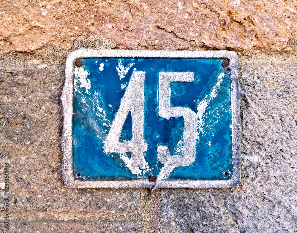 45 (forty-five) a dented plate with house number on a stone wall. 45 (forty-five) a dented plate with house number on a stone wall.