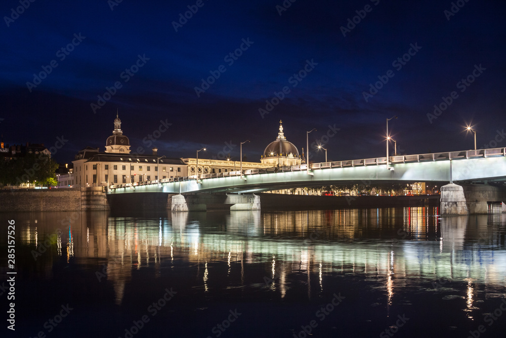 Pont de la Guillotiere bridge in Lyon, France over a panorama of the riverbank of the Rhone river (Quais de Rhone) at night with the main monuments of the old Lyon in background