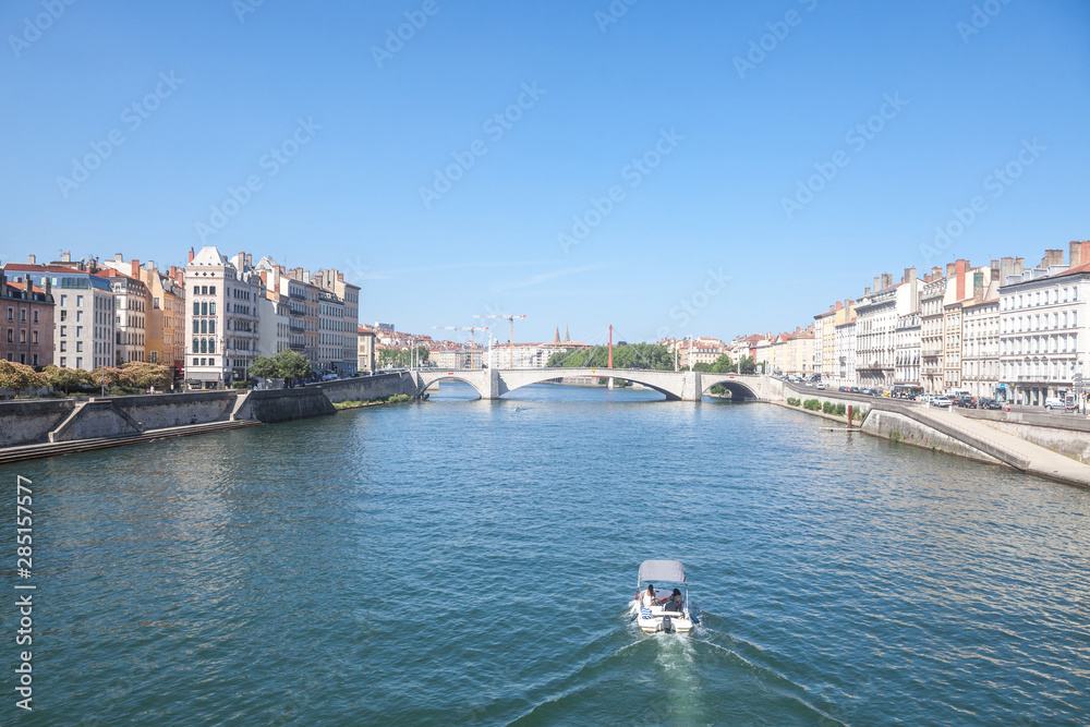 Boat approaching Pont Bonaparte bridge of Saone river near the Quais de Saone riverbank and riverside in the city center of Lyon during a summer afternoon