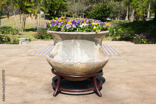 Decoration large pot with flowers in public park background. Big clay pot with decorative flowers and metal stand in the garden