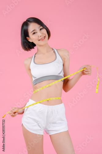 Healthy woman standing holdding tape measure and showing her beautiful body in home on pink backgrounds, Healthy concept, Diet concept