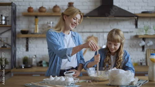 Mom and daughter bake pancakes in the kitchen together. girl helps her mom get dough. 4K