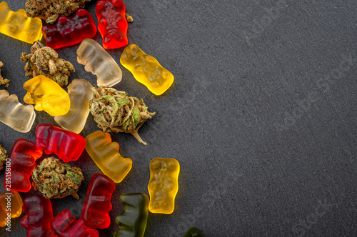Cannabis edibles, medical marijuana, CBD infused gummies and edible pot concept theme with close up on colorful gummy bears and weed buds on dark background with copy space photo