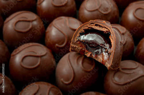 Sweet confectionery and candy indulgence concept theme with close up on a bitten cherry filled chocolate praline on top of many other delicious pralines with copy space