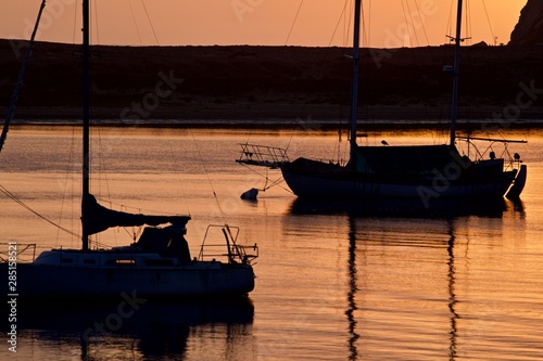 Fototapeta Naklejka Na Ścianę i Meble -  two sailboats are moored in a harbor at morro bay on the central california coast during a pink sunset