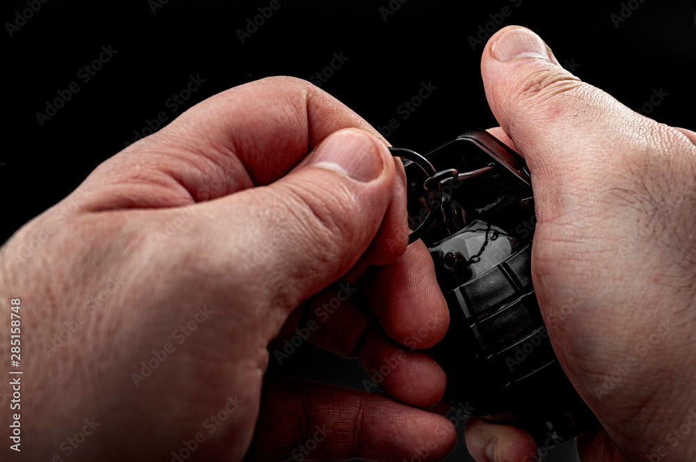 Stressful modern warfare, explosive weapon and escalating tension in military conflict concept theme with close up on solder hands that pull the pin on grenade isolated on black background Stressful modern warfare, explosive weapon and escalating tension in military conflict concept theme with close up on solder hands that pull the pin on grenade isolated on black background