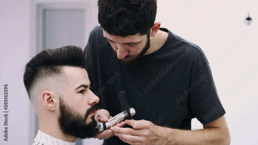attractive businessman sitting in a chair while getting a modern and stylish haircut from a barber at the hair salon
