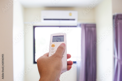 Man adusting the temperature of air conditioner by using a remote control.