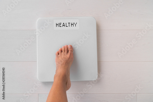 Happy weight loss woman stepping on scale weighting healthy weight after diet goal challenge. Top view of foot step on balance showing screen with good news text. photo