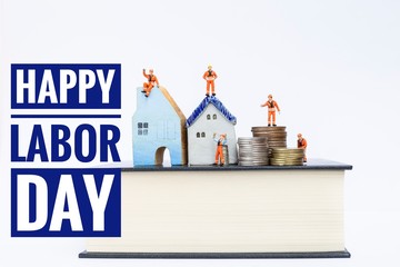 Happy Labor Day with Miniature worker in safety suit on coins stack and miniature house on the thick book isolate on white background, real estate business, construction business, house maintenance