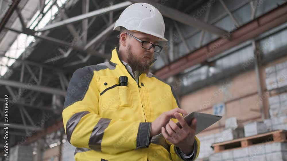 Worker male warehouse worker engineer man in a helmet working on the construction site of the warehouse, tablet computer, checking the warehouse, inspection of goods Worker male warehouse worker engineer man in a helmet working on the construction site of the warehouse, tablet computer, checking the warehouse, inspection of goods