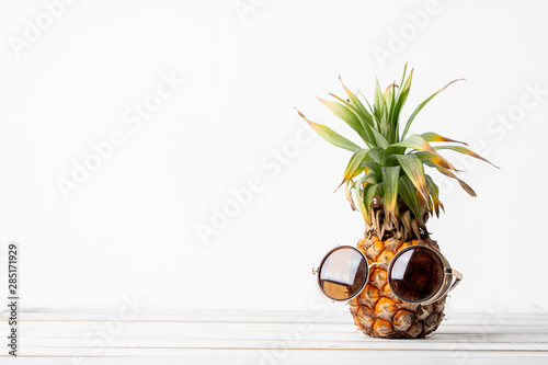 Pineapple with sunglasses on wooded table white background.
