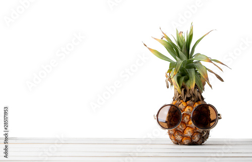 Pineapple with sunglasses on wooded table white background.