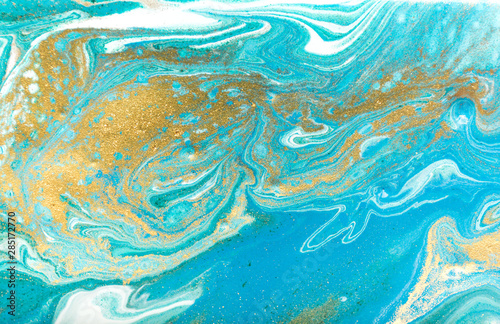 Liquid blue abstract marbling texture with golden glitter and glare of light.