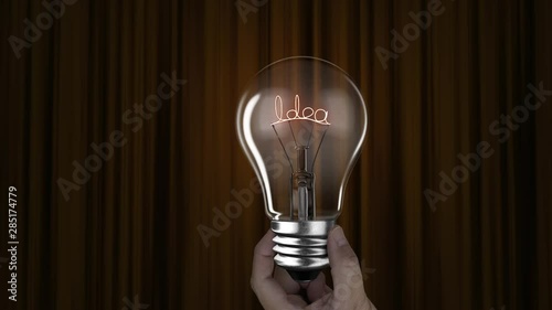 Hand holding lighting bulb lamp with idea words on gold yellow curtain background, 3D rendering animation, macro view