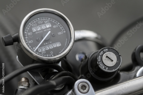 Close up picture of the vintage style of dark speedometer gauge and old on-off ignition switch from retro classic motorcycle background.