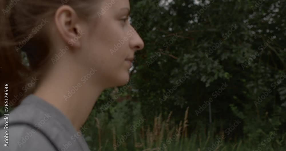 SIDE VIEW TRACKING CRANE SHOT of a beautiful young woman walking on a path in the countryside with purple flowers in the background.