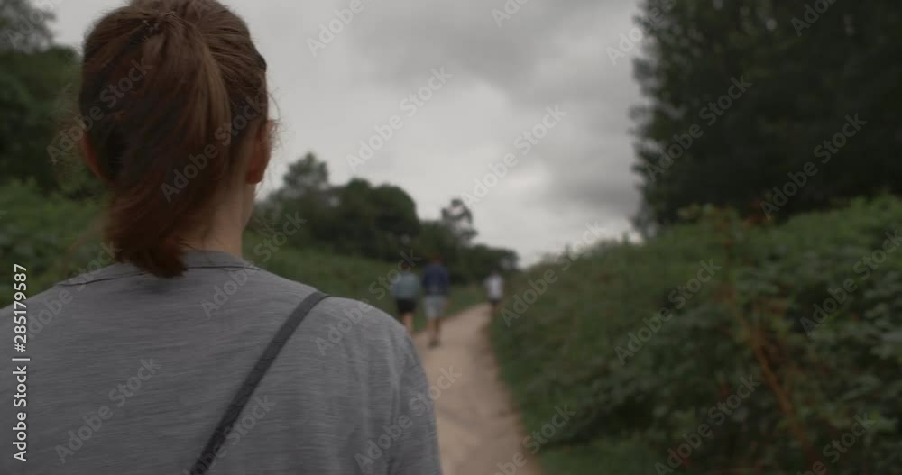 A TRACKING SHOT over the shoulder of a woman walking on a countryside path on a cloudy day. A TRACKING SHOT over the shoulder of a woman walking on a countryside path on a cloudy day.