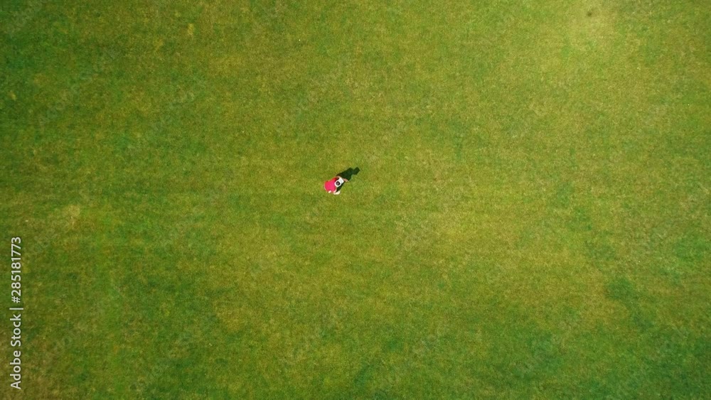 Aerial view of man, who using a VR headset and playing a virtual game in the park. Young guy in helmet experiencing augmented reality on the background of nature. 4K drone footage. Aerial view of man, who using a VR headset and playing a virtual game in the park. Young guy in helmet experiencing augmented reality on the background of nature. 4K drone footage.
